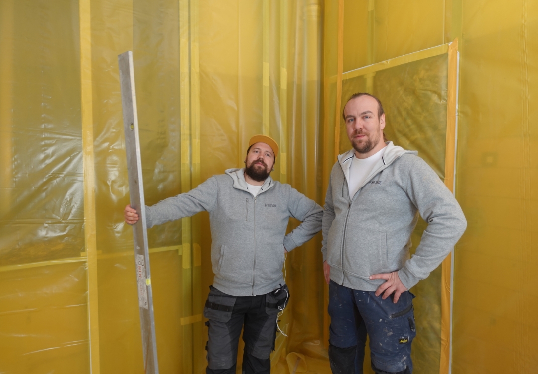Wykonawcy z Ekipa Remontowa Siniat stojący na tle ściany z zainstalowaną żółtą folią paroizolacyjną przymocowaną do profili stalowych nida CD.