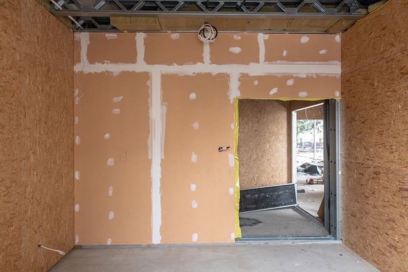 Wnętrze pokoju w budynku w czasie budowy. Blado pomarańczowe ściany. Po prawej stronie znajduje się przejście do innego pokoju.